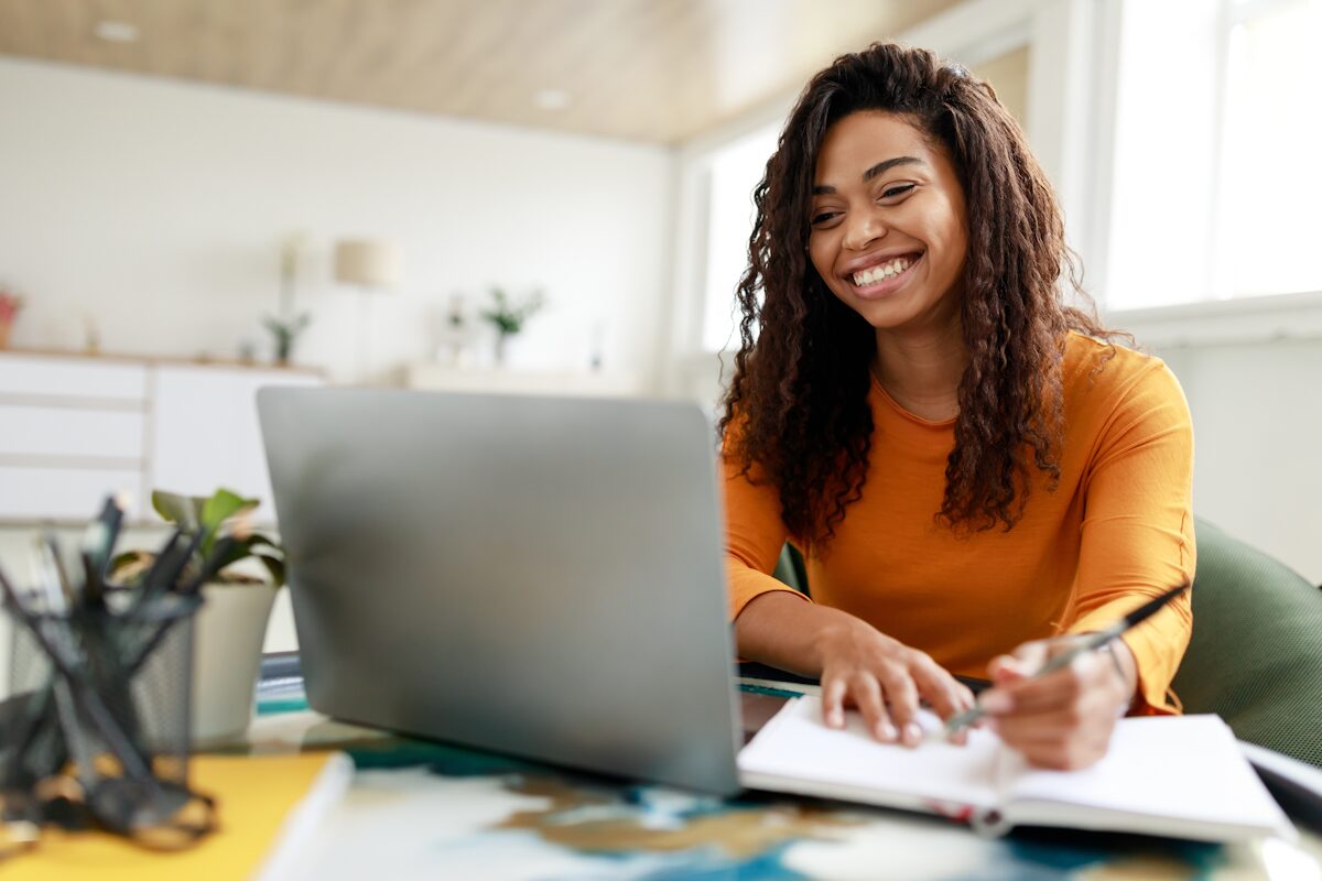 Smiling woman studying using a laptop, pen and paper